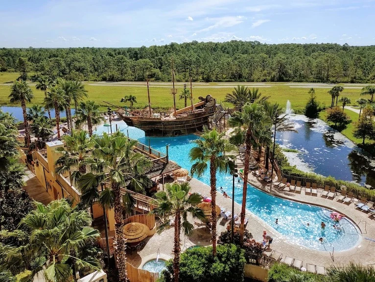 Resort pool with a pirate ship feature, palm trees and a surrounding waterway