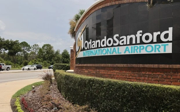 Orlando Sanford International Airport entrance sign beside landscaped grounds and the access road